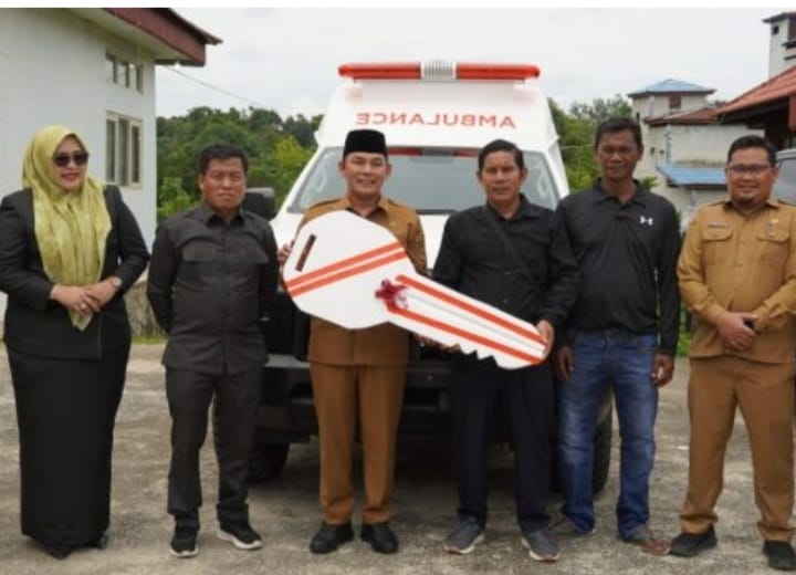 Rahmanto Muhidin dan Anwari berdiri di samping ambulans putih berstrip merah, latar belakang kelompok pejabat mengenakan pakaian formal di acara Musrenbang Laung Tuhup, Puruk Cahu.