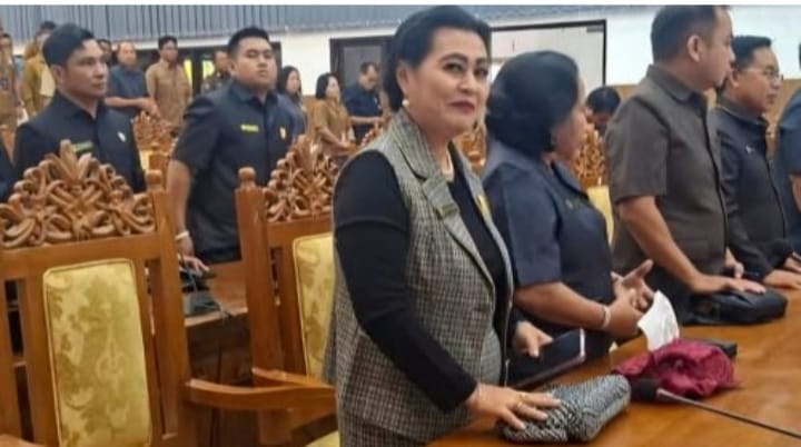 Rayaniatie Djangkan mengenakan rompi kotak abu-abu dan busana hitam, berada di ruangan rapat dengan kursi ukir kayu, saat DPRD Gunung Mas membahas LKPJ tahun anggaran 2025.