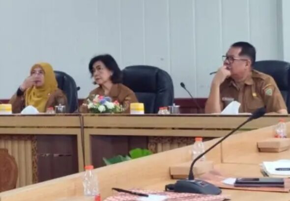 Rapat persiapan Hari Jadi ke-69 Kalimantan Tengah, Linae Victoria Aden duduk di meja kayu dengan mikrofon, suasana kantor pemerintah