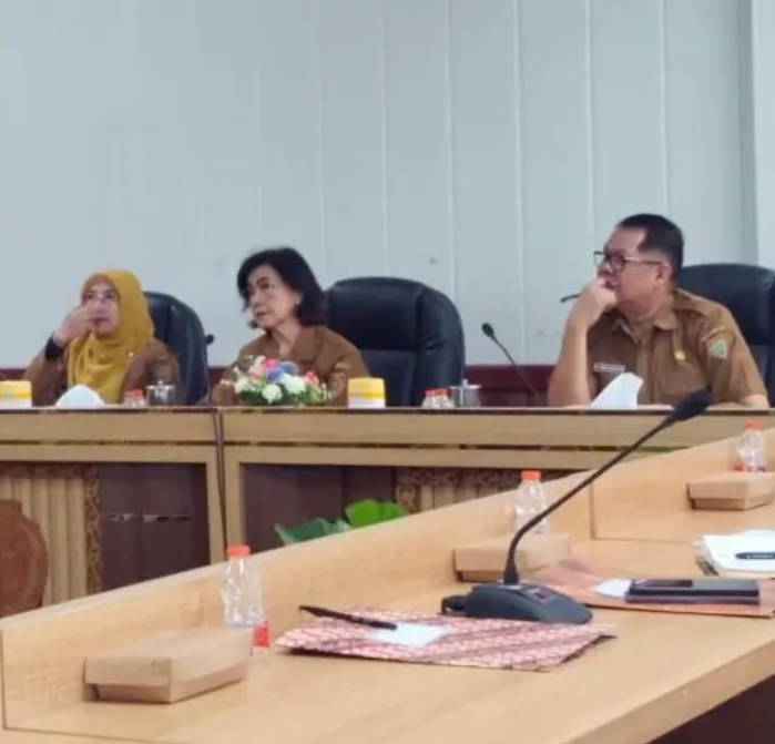 Rapat persiapan Hari Jadi ke-69 Kalimantan Tengah, Linae Victoria Aden duduk di meja kayu dengan mikrofon, suasana kantor pemerintah